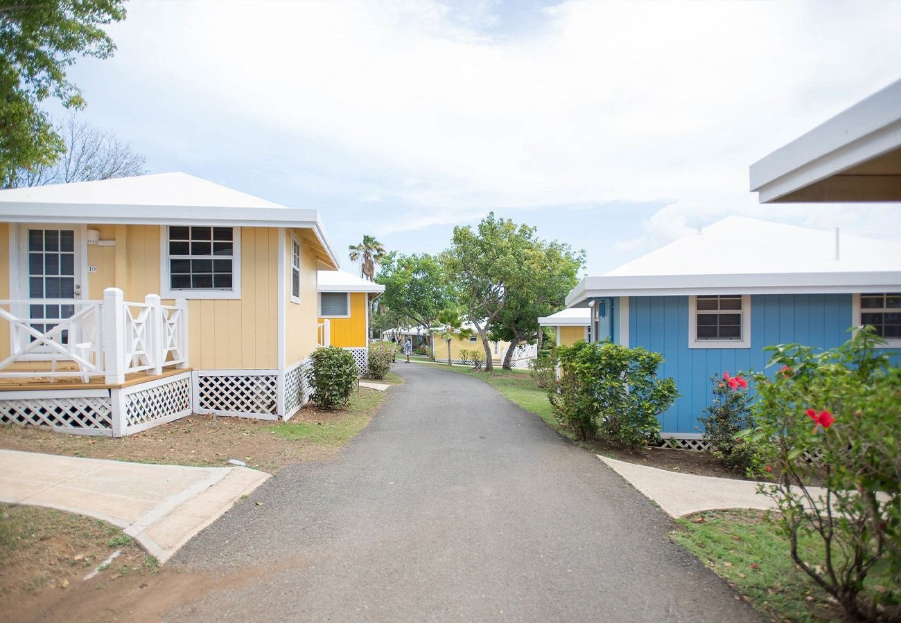 A yellow house and a blue house are next to each other on a dirt road.