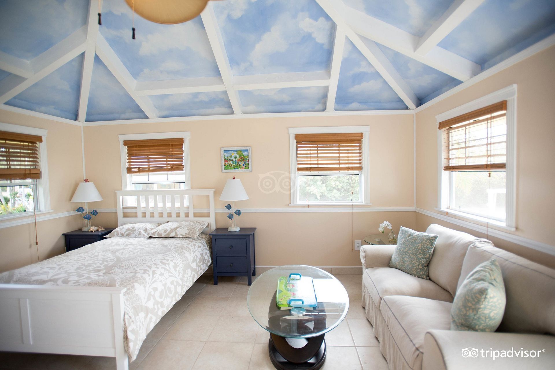 A bedroom with a couch and a bed with a blue sky painted on the ceiling