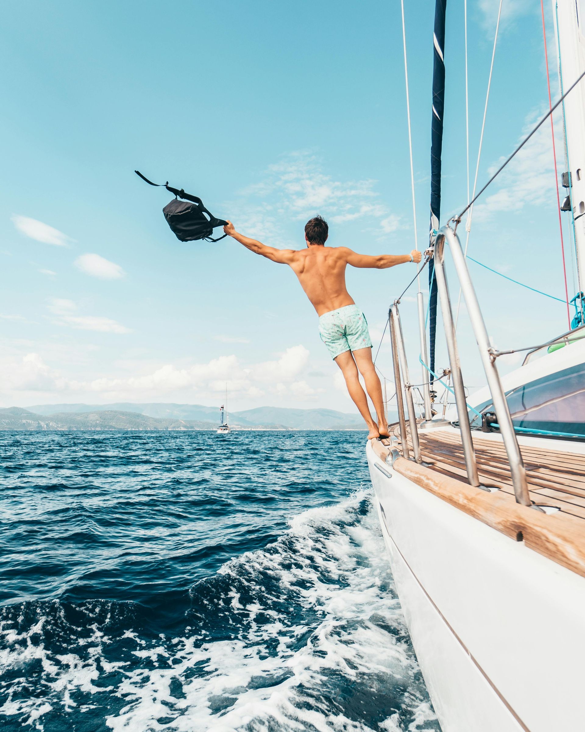 A man is jumping off a sailboat into the ocean.