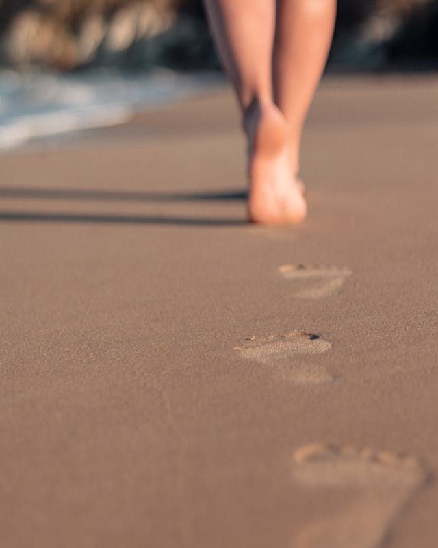 Bare feet walking on wet sand, leaving footprints near the ocean, demonstrating somatic regulation.