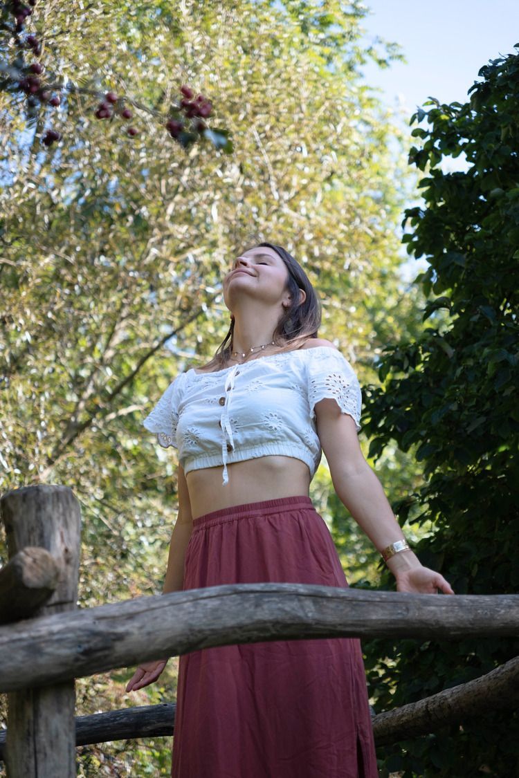 Woman in white top and red skirt gazes upward in a park.
