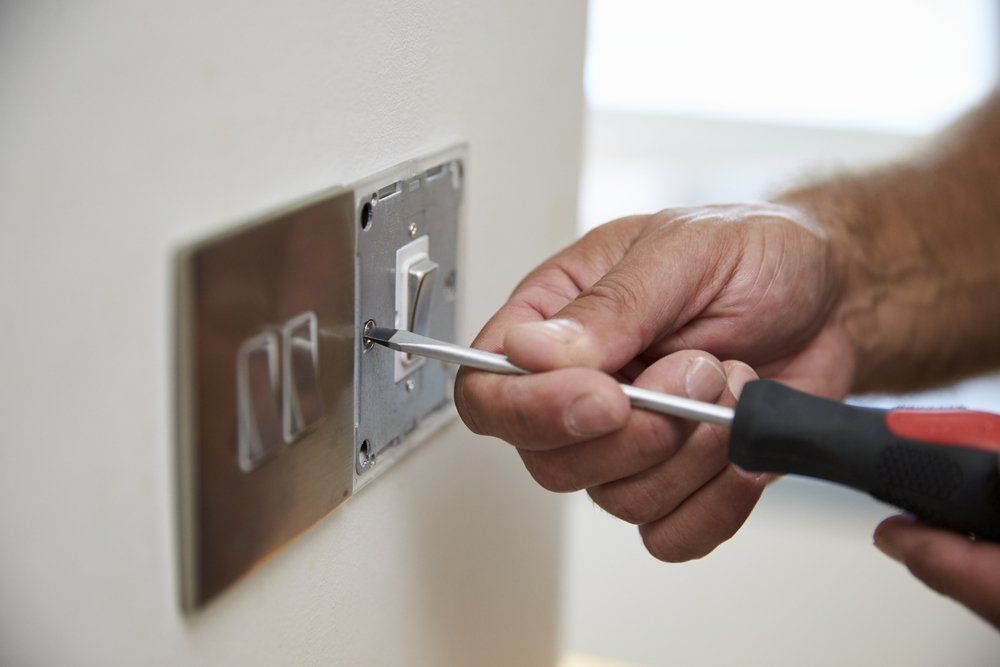 A Person Is Fixing A Light Switch With A Screwdriver — Peter Jones Electrical In Bonny Hills, NSW
