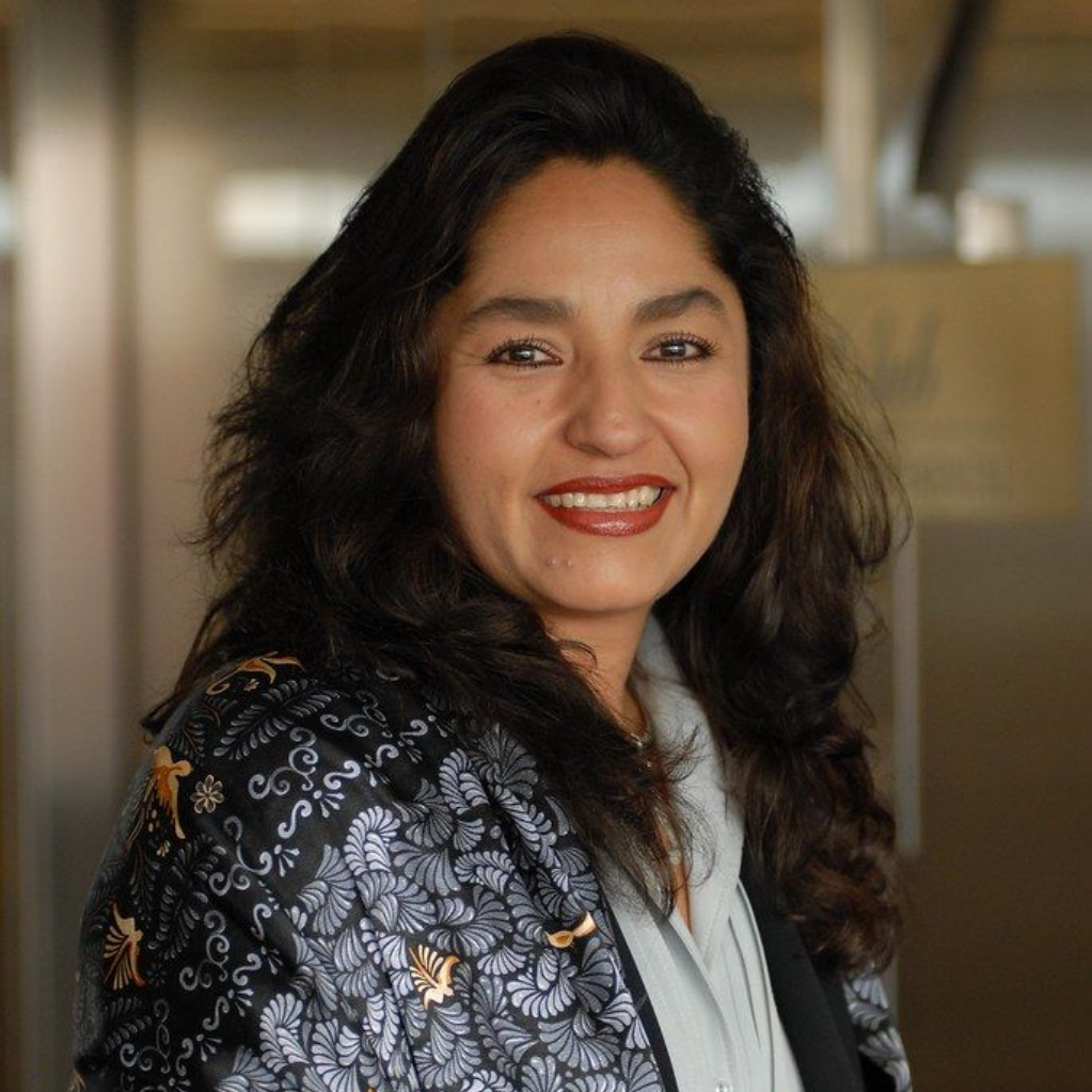 Una mujer con una chaqueta estampada sonríe en un interior con un suave fondo de oficina detrás de ella.