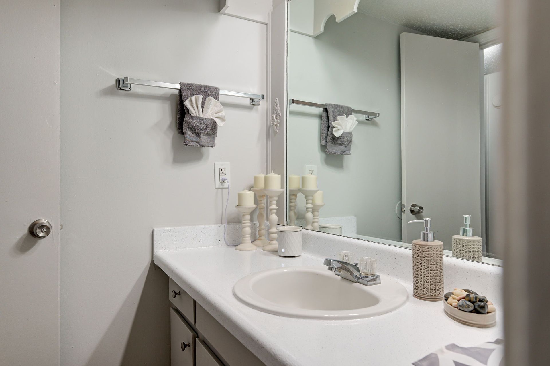 A bathroom with a sink , mirror and towels hanging on the wall.