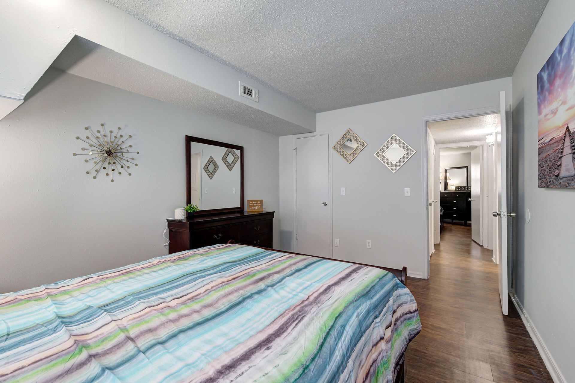 A bedroom with a bed , dresser , mirror and painting on the wall.