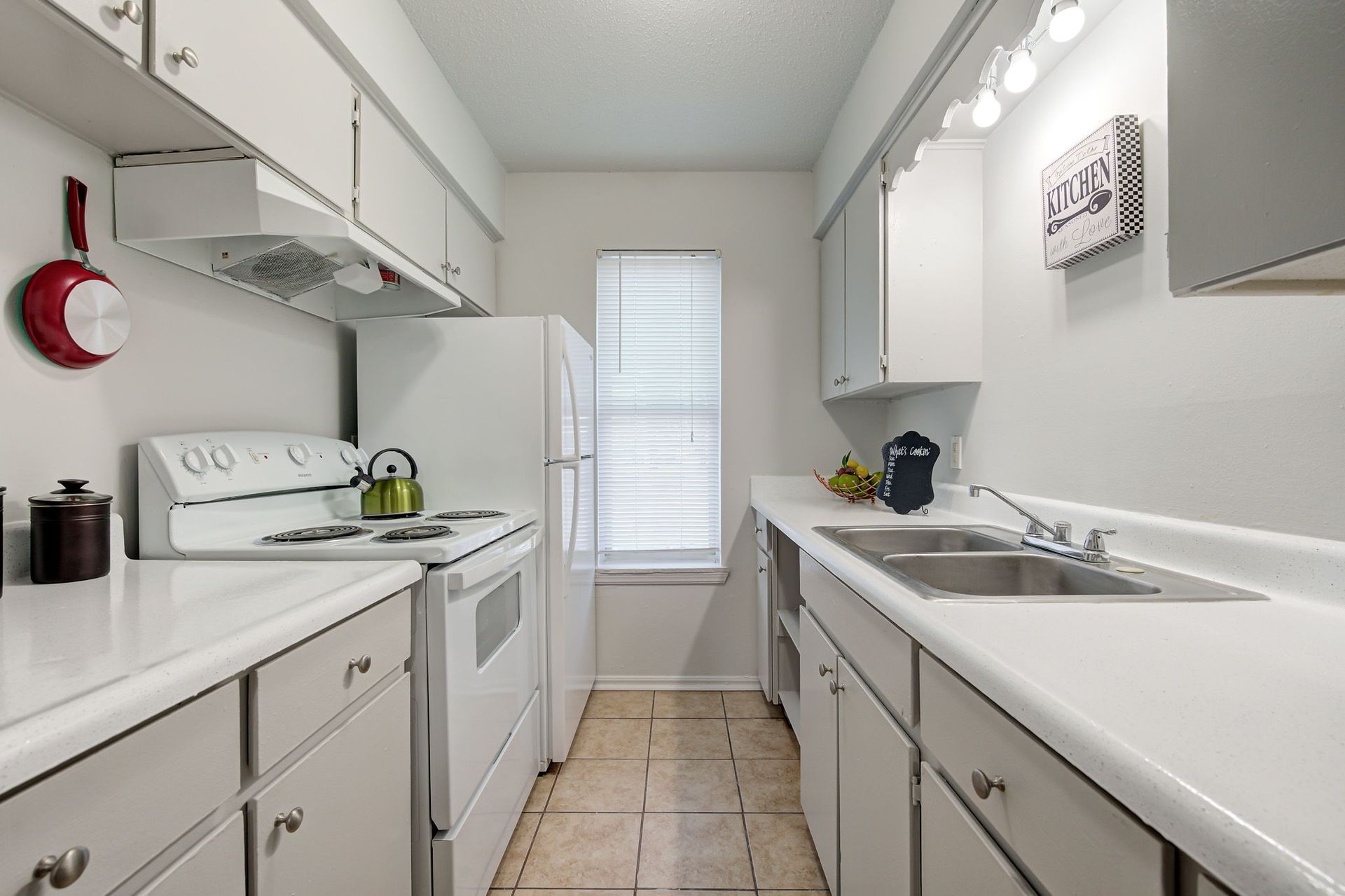 A kitchen with white cabinets , a stove , a refrigerator , a sink and a window.