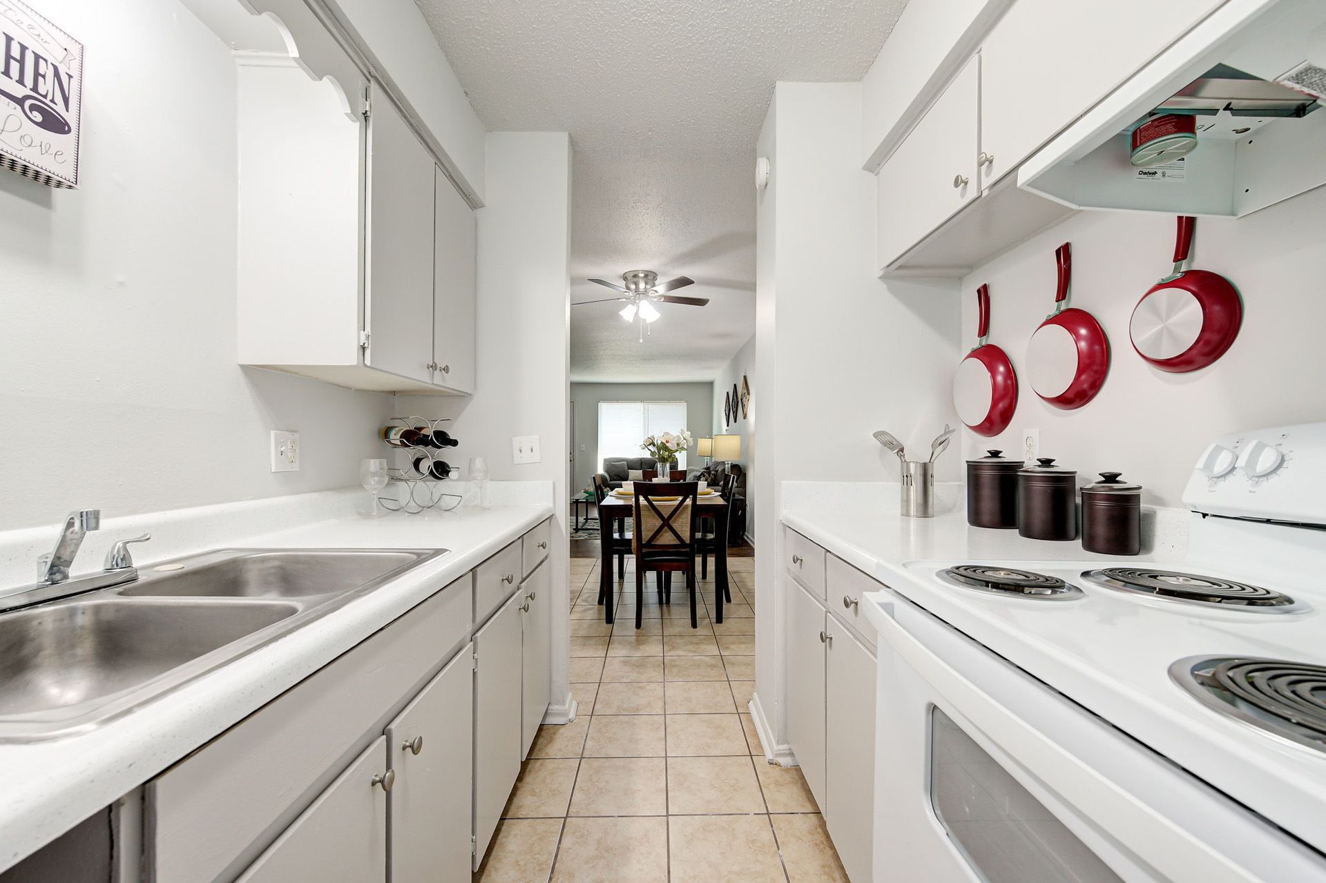 A kitchen with white cabinets and red pots and pans hanging on the wall.