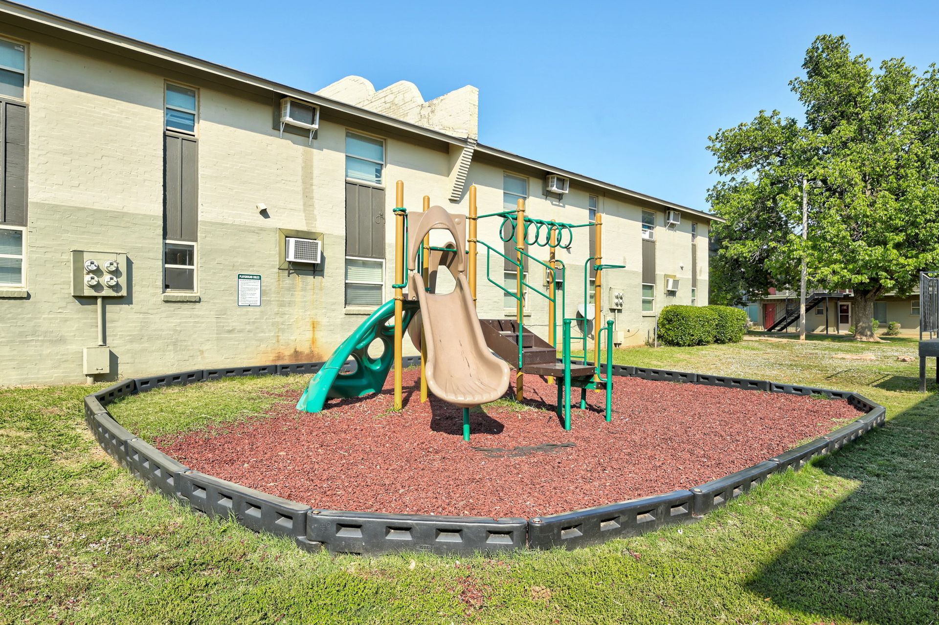 A playground with a slide and a swing set in front of a building.