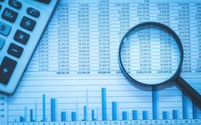A magnifying glass is sitting on top of a spreadsheet next to a calculator.