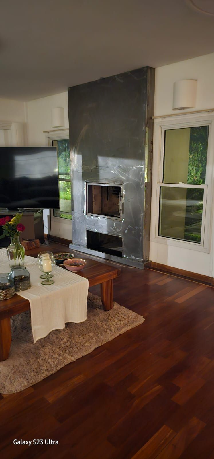 Sala de estar con gran chimenea gris y suelos de madera oscura.