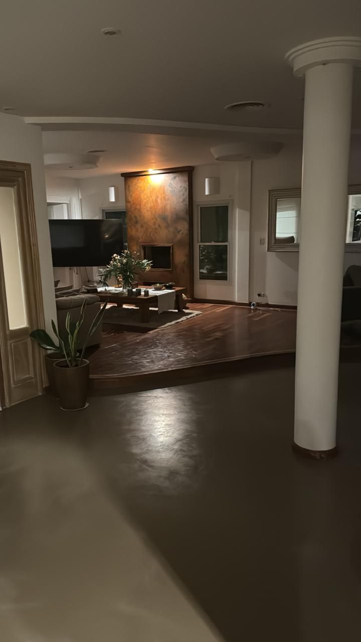 Vista interior de un espacio habitable con piso de madera elevado, chimenea y una gran columna blanca.