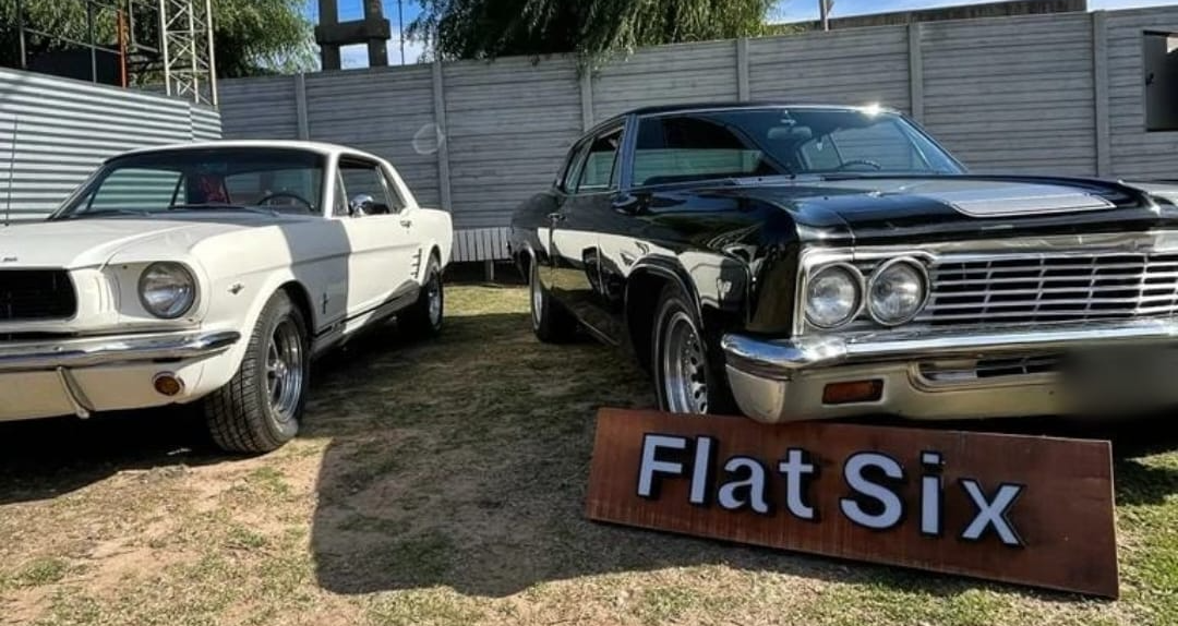Autos clásicos blancos y negros estacionados al aire libre junto a un cartel que dice 
