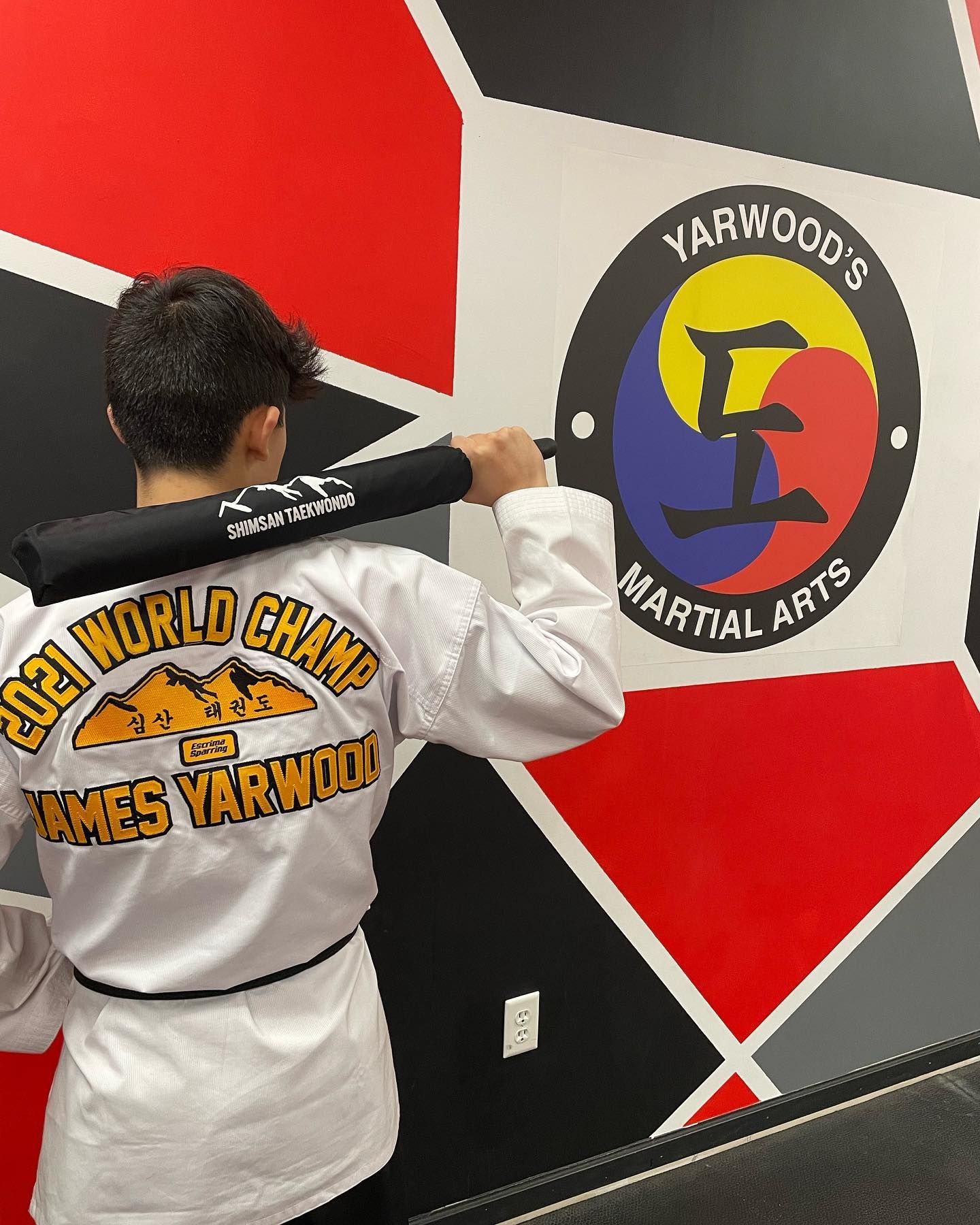 a man in a martial arts uniform holds a bat in front of a wall that says yarwood 's martial arts