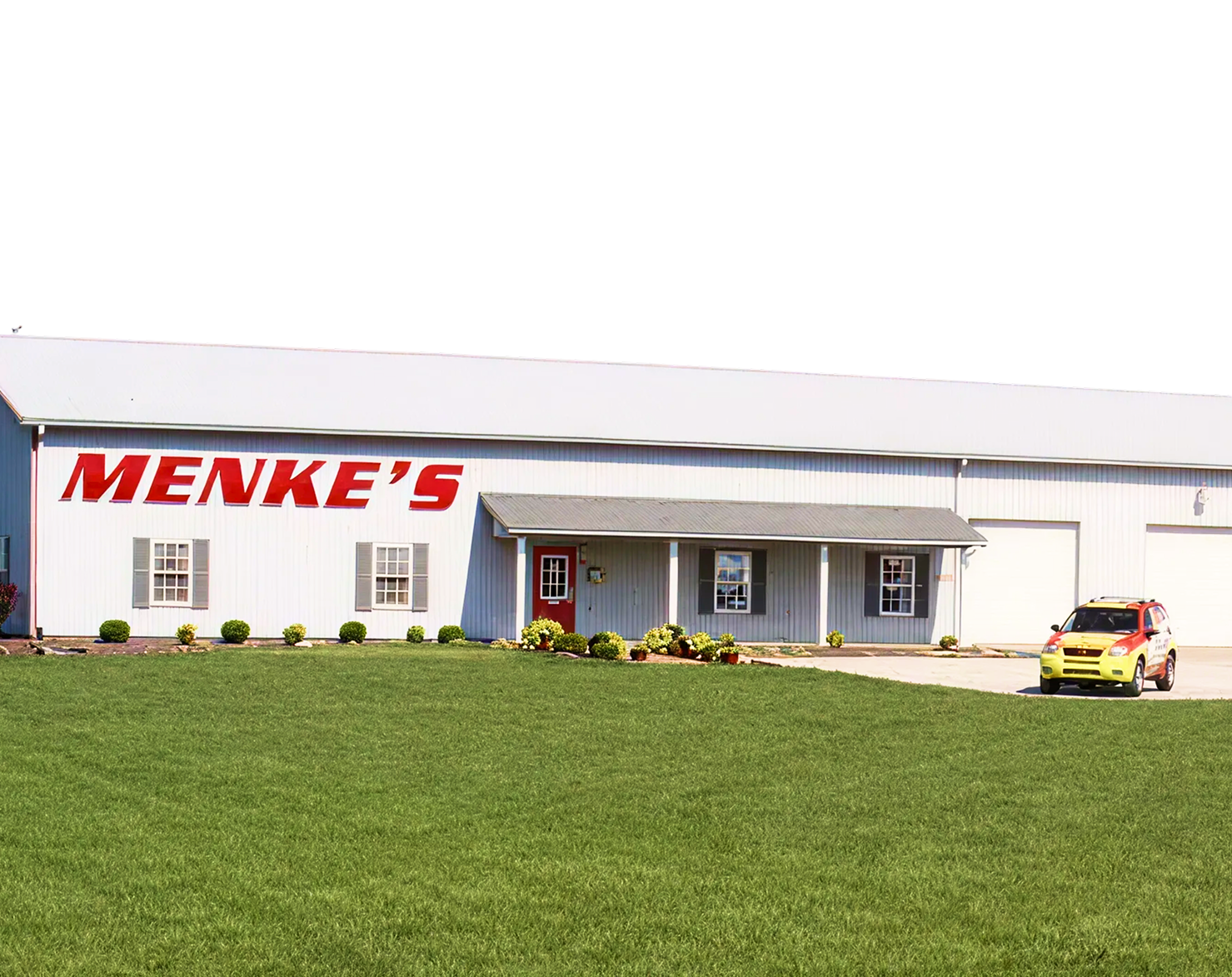 Menke's building with red lettering, white exterior, red door, and yellow vehicle in front. | Menke's Automotive Repair