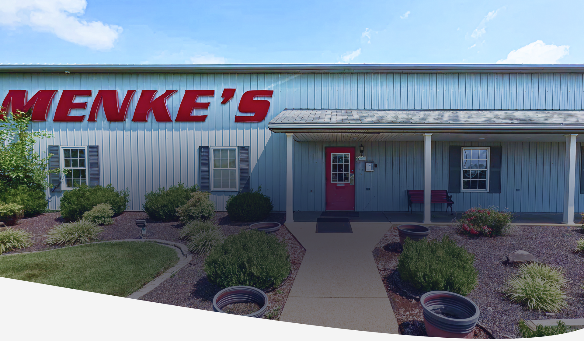 Exterior of Menke's building with red sign, pink door, and landscaping. | Menke's Automotive Repair