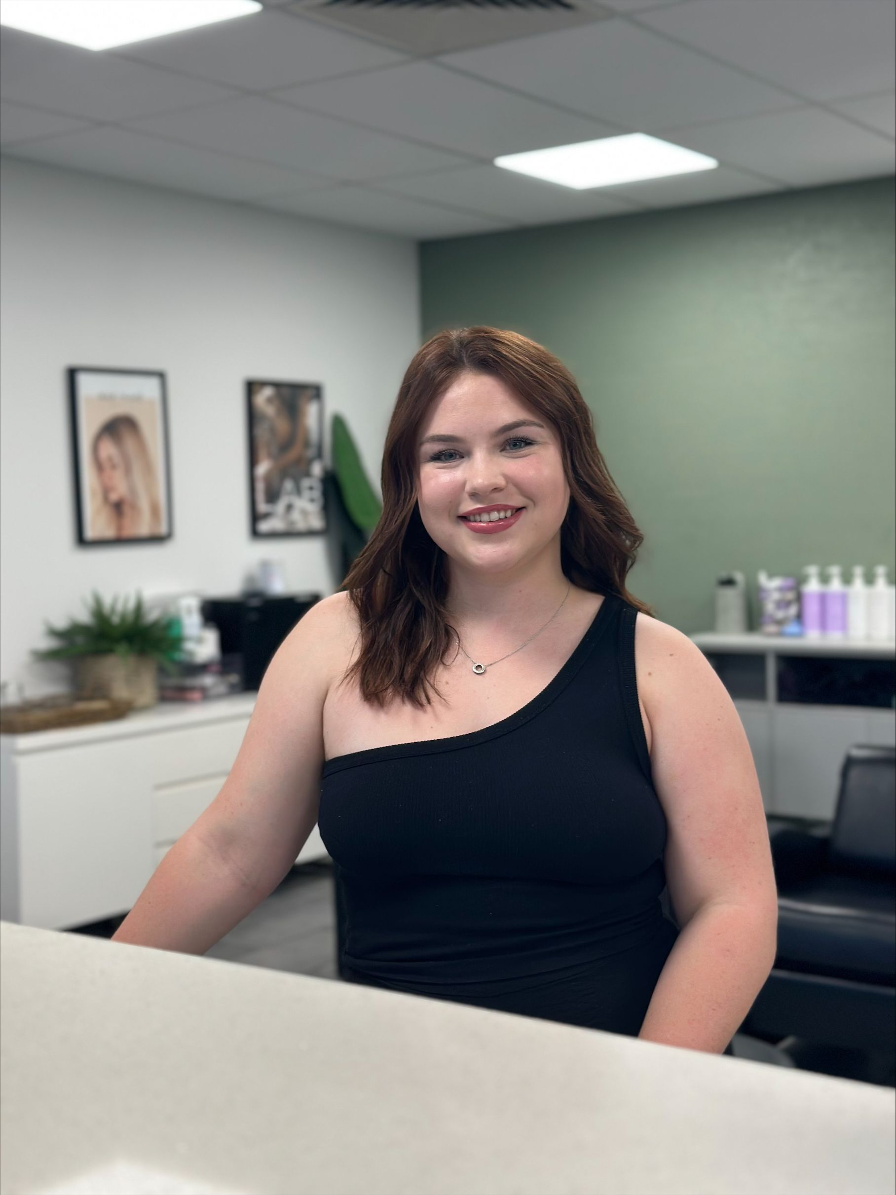 A woman in a black tank top is sitting at a counter in a salon — Fusion Hair In Woree, QLD