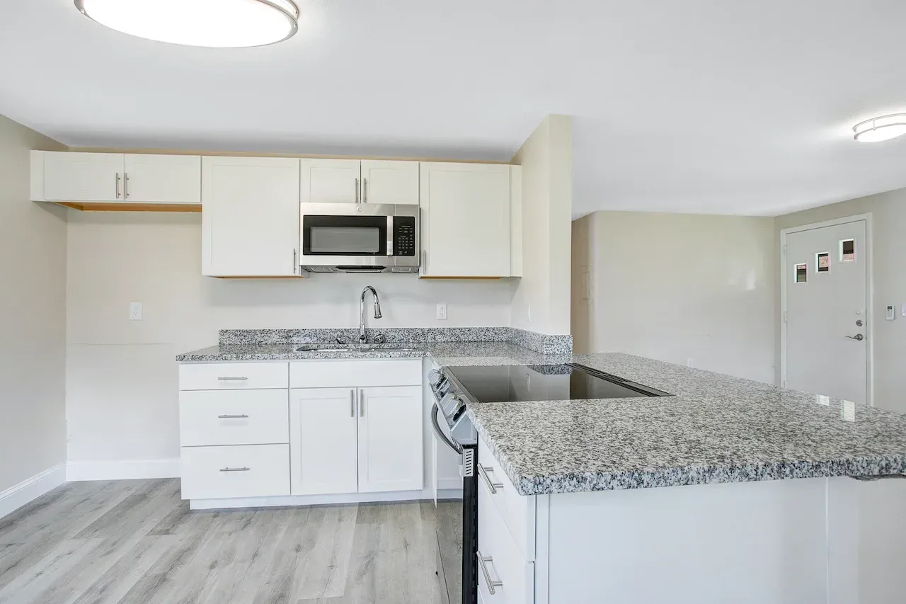 A kitchen with granite counter tops , white cabinets , stainless steel appliances and a microwave.