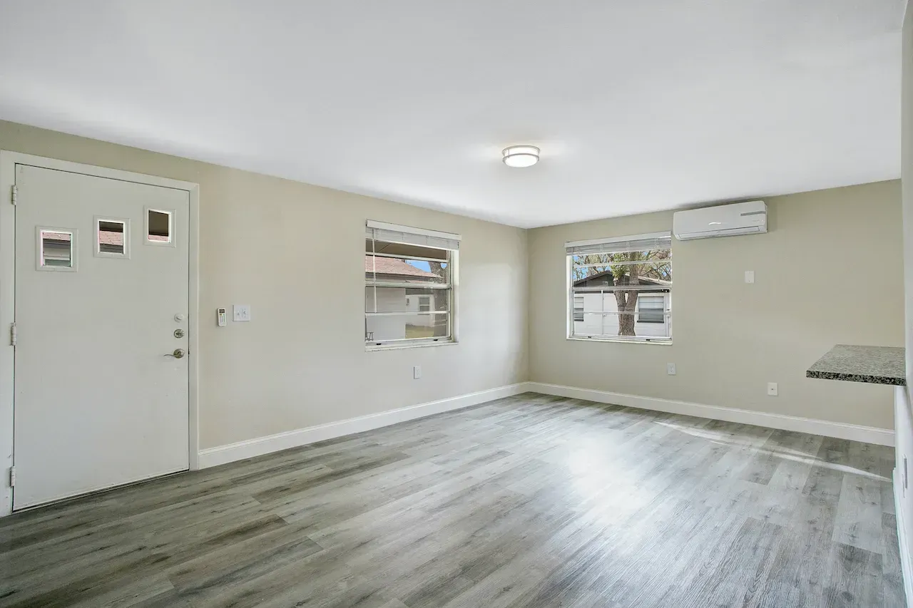 An empty living room with hardwood floors and a white door.