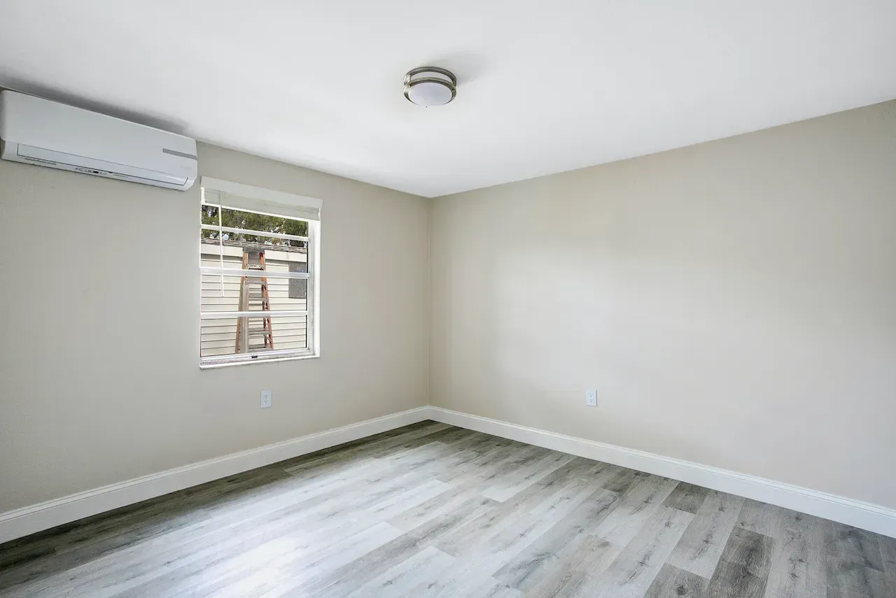 An empty bedroom with hardwood floors and a window.
