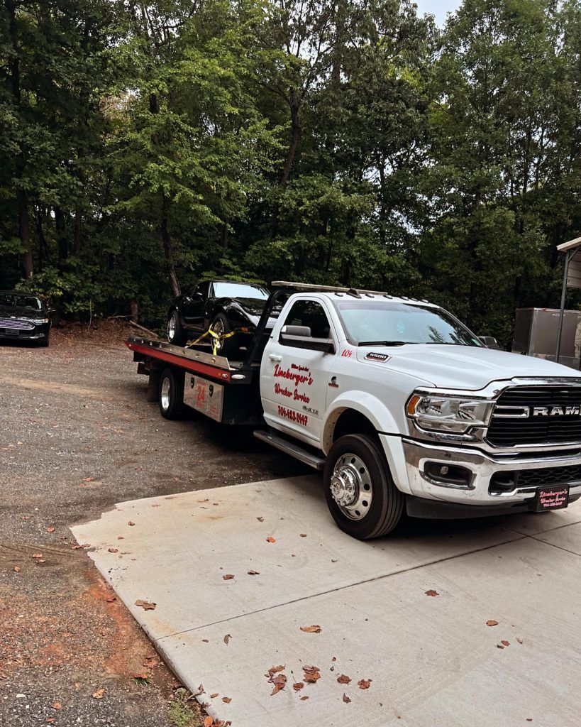 A white tow truck is towing a car in a driveway.