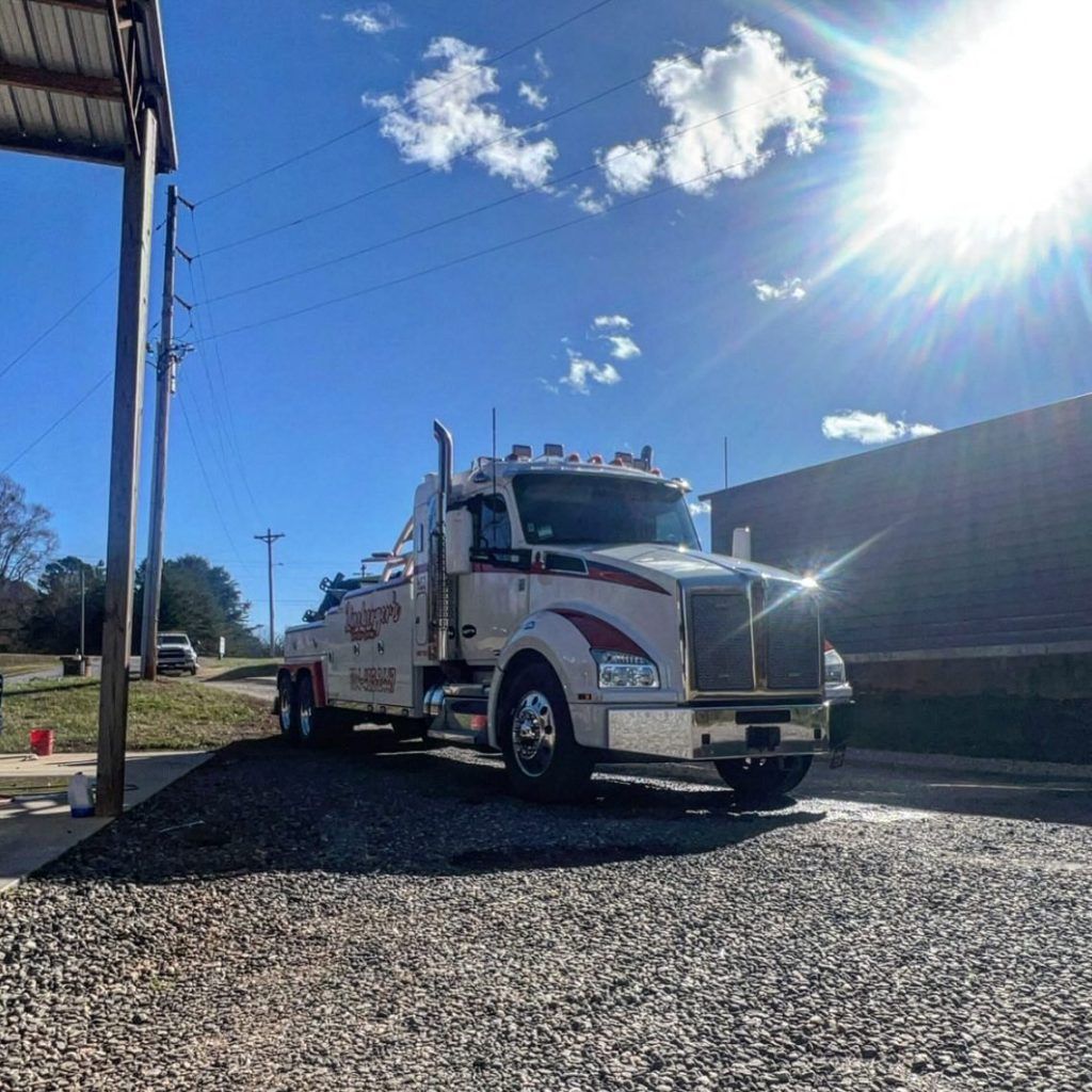 A white tow truck is parked on gravel in front of a building.