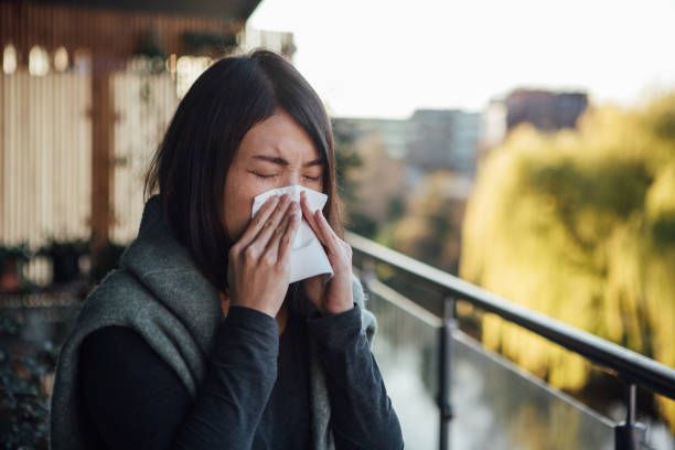 A woman is blowing her nose into a napkin on a balcony.