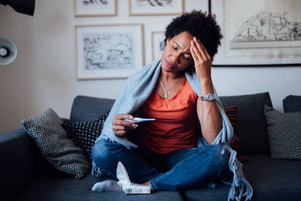 A woman is sitting on a couch with a thermometer in her hand.