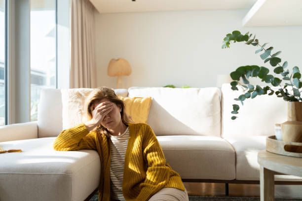 A woman is sitting on a couch covering her face with her hand.