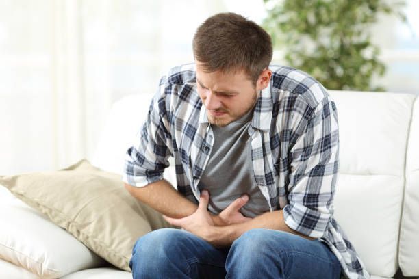 A man is sitting on a couch holding his stomach in pain.