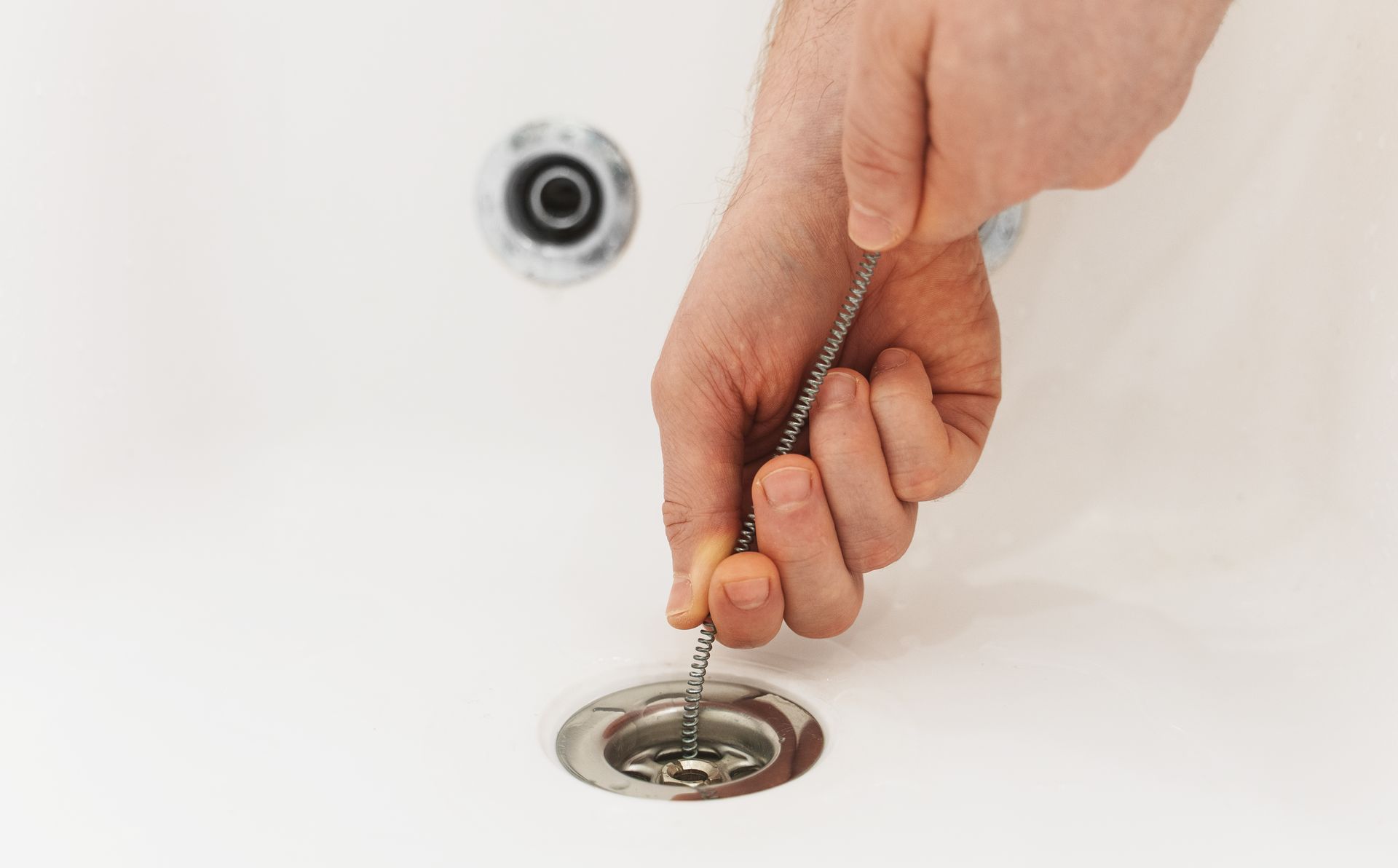 Hand holding a plug above a bathroom sink drain and faucet hole
