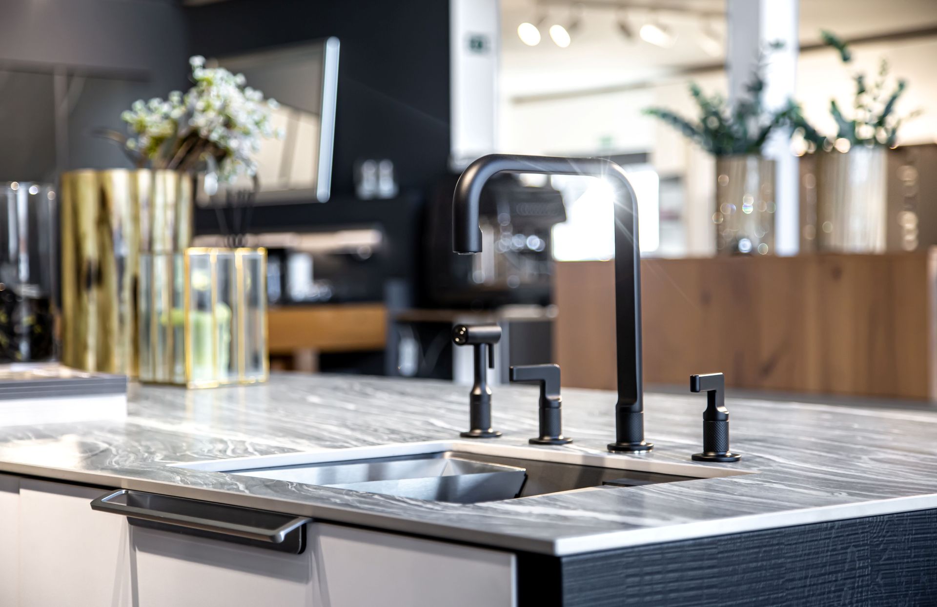 Black faucet and soap dispensers on a marble countertop with a stainless steel sink, in a kitchen setting.