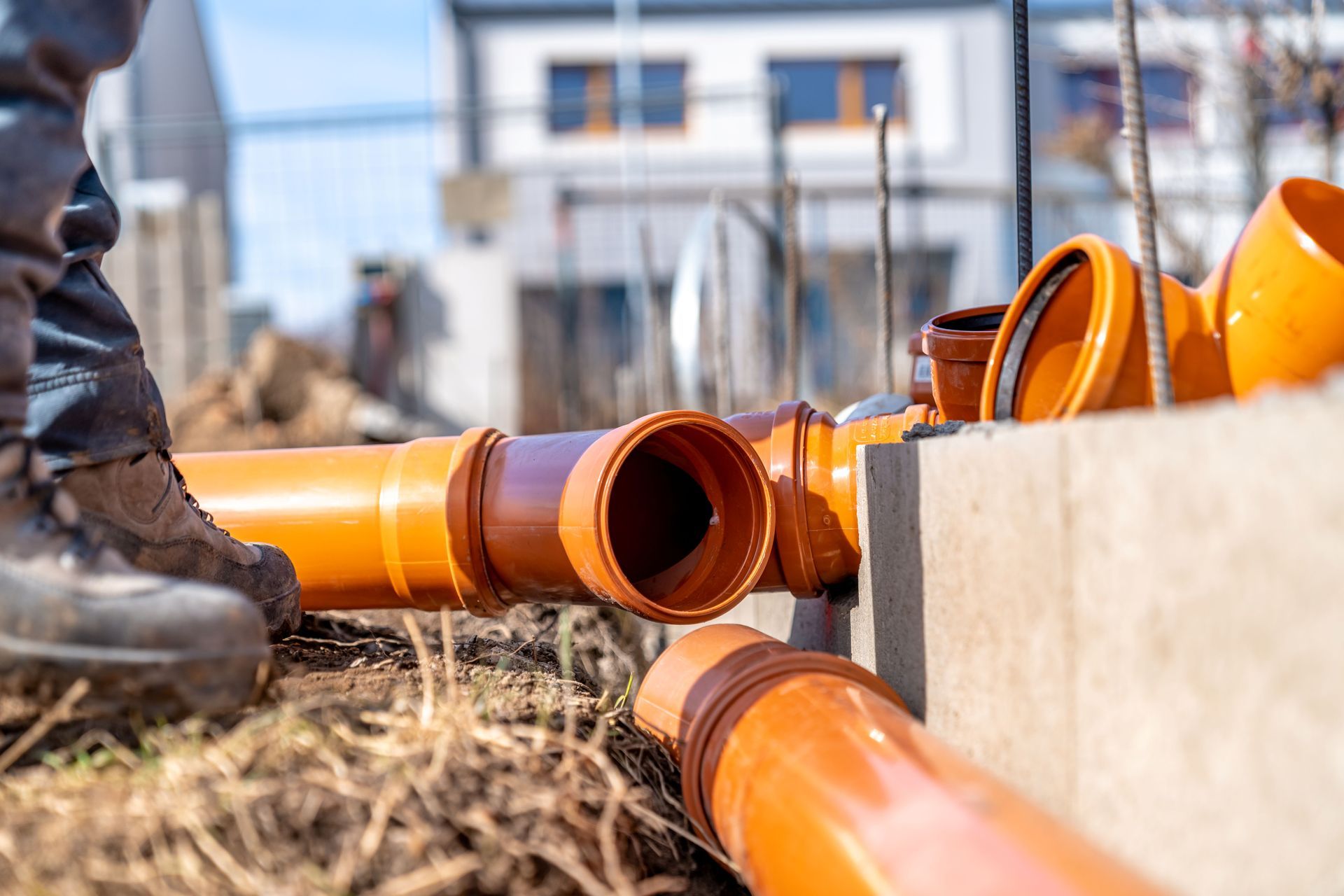 Construction worker installing orange pipes in a trench at a building site.