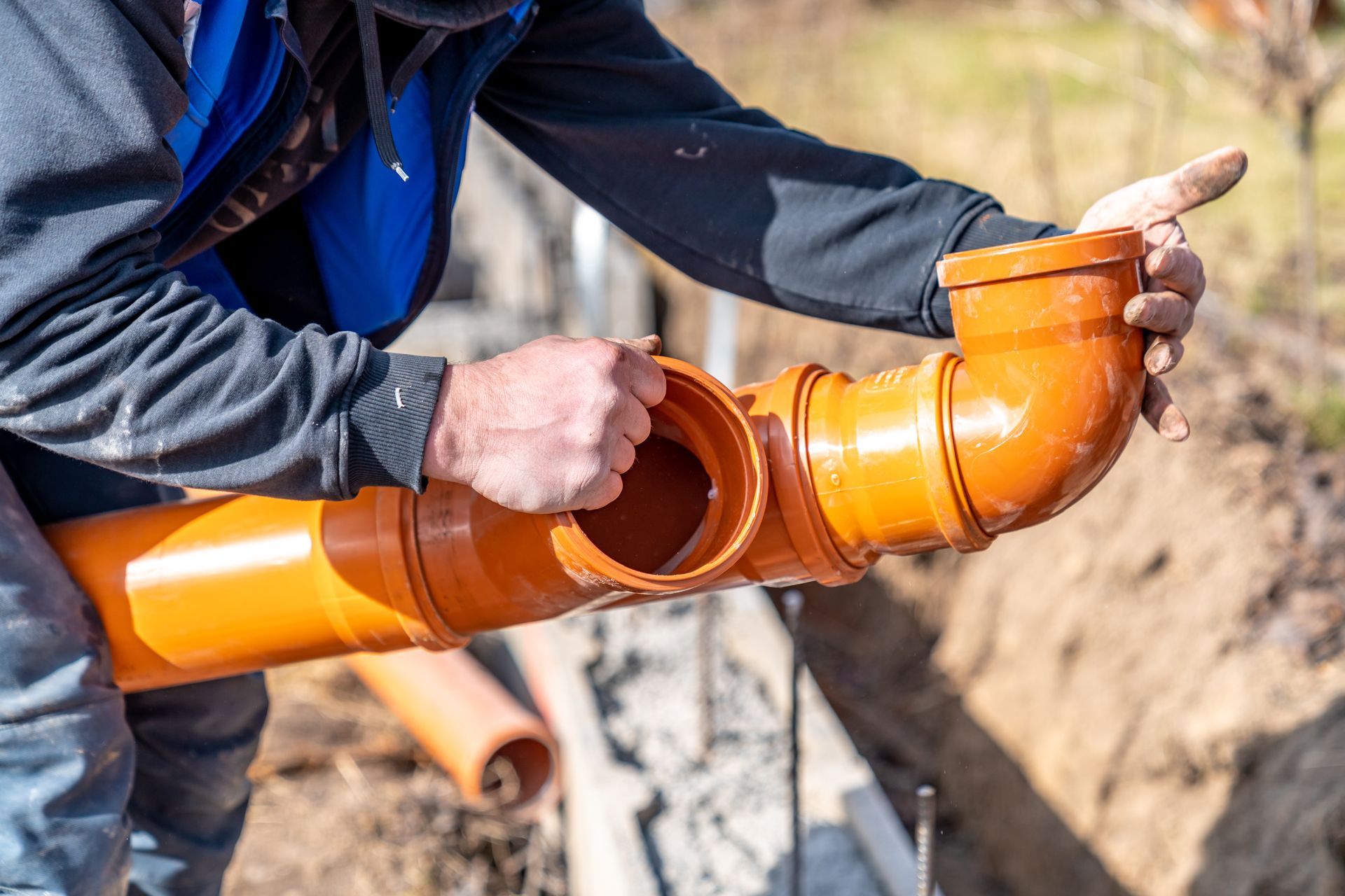 Worker fitting orange PVC pipes at a construction site