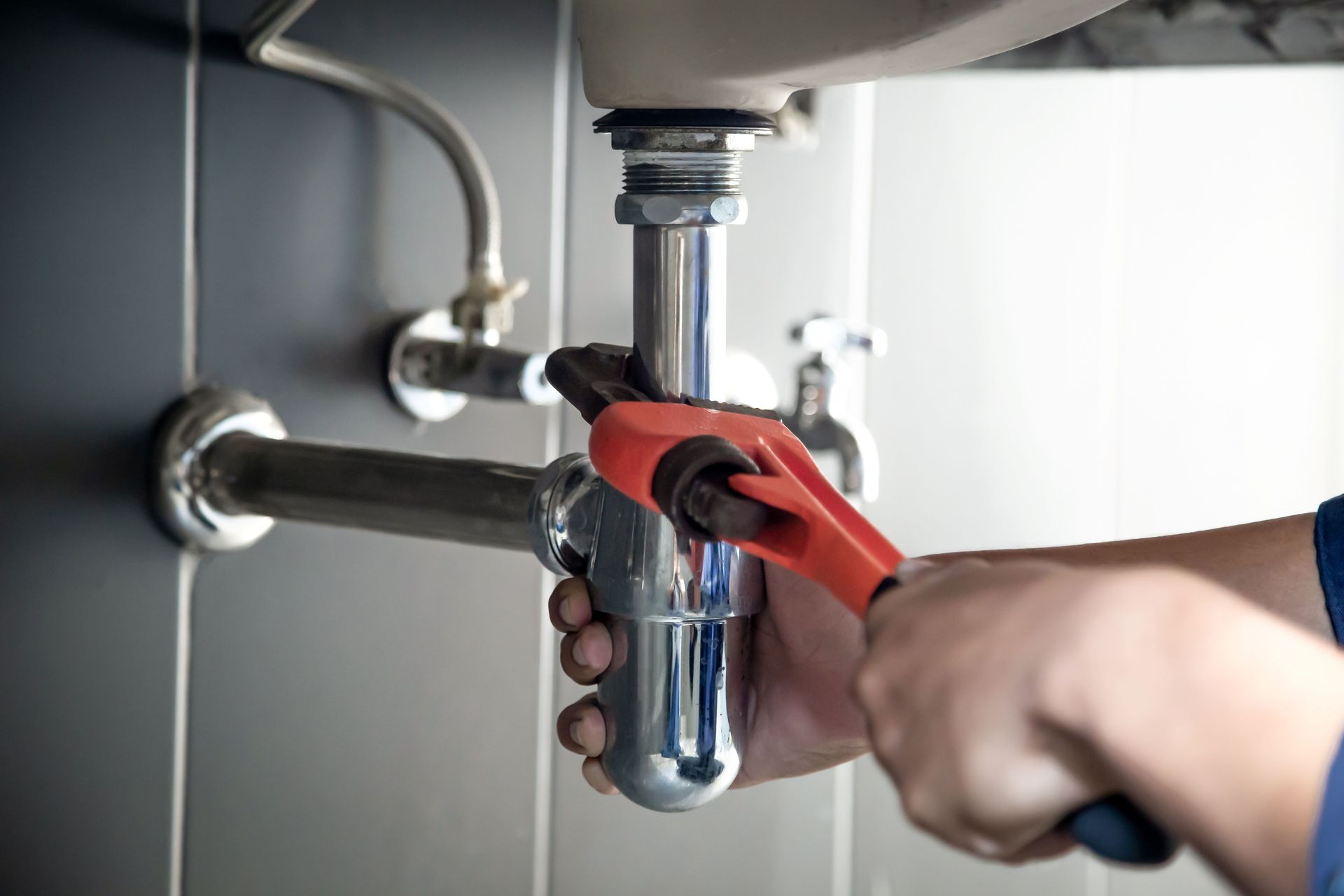 Plumber using a wrench to tighten a pipe under a sink.