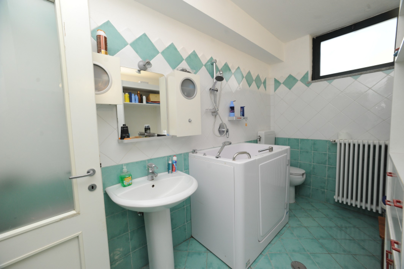 Bagno con vasca, lavandino e WC accessibili. Piastrelle turchesi e bianche.