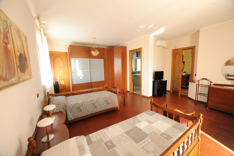 Ampia camera da letto con due letti singoli, mobili in legno e accesso al bagno.