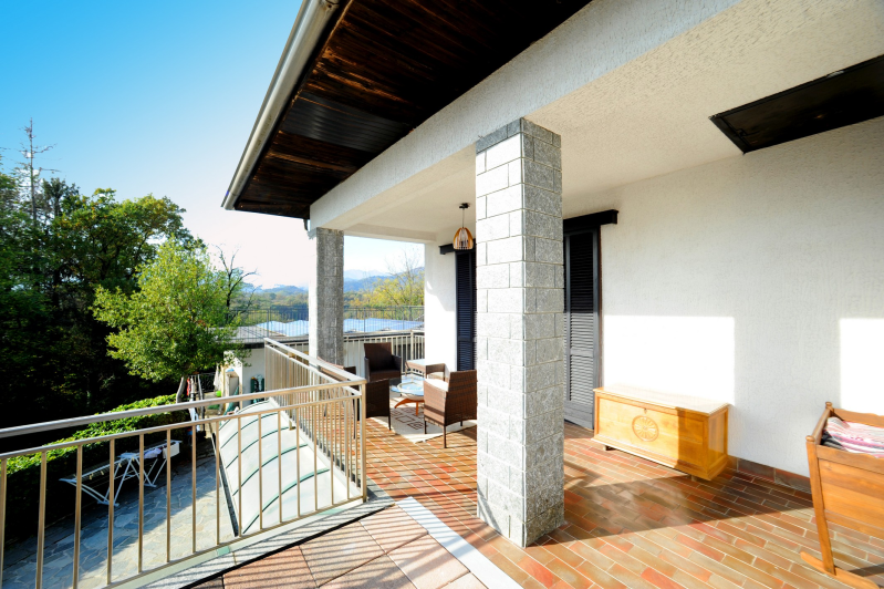 Balcone con posti a sedere all'aperto, pavimento in mattoni, colonne in pietra, vista sugli alberi e vista panoramica.