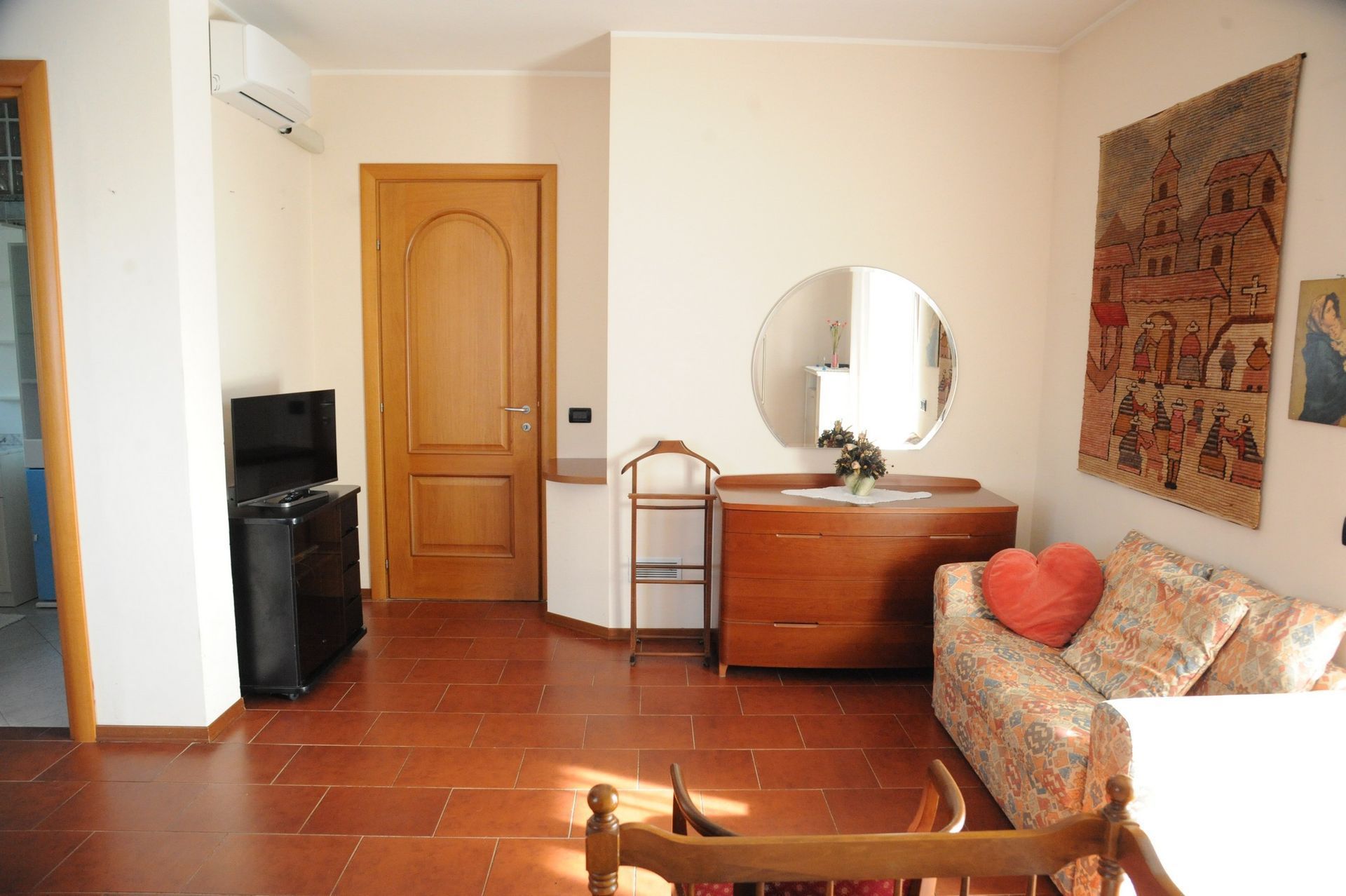 Accogliente soggiorno con pavimento piastrellato, porta in legno, divano e arazzo decorativo.