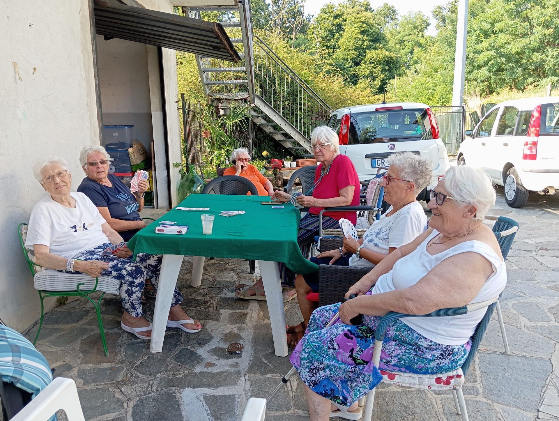 Un gruppo di anziani gioca a carte all'aperto, seduti a un tavolo.