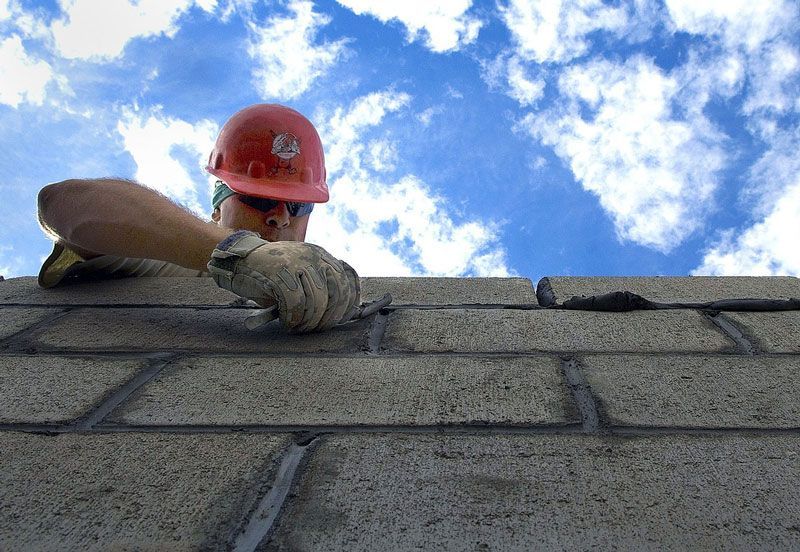 A man wearing a hard hat and gloves is working on a brick wall.