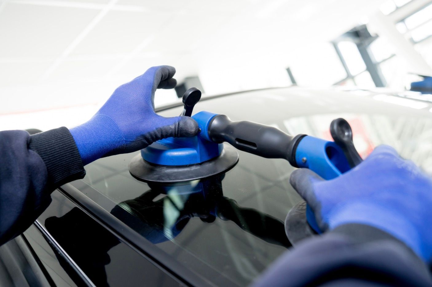 Hands in blue gloves using a suction tool on a car windshield.