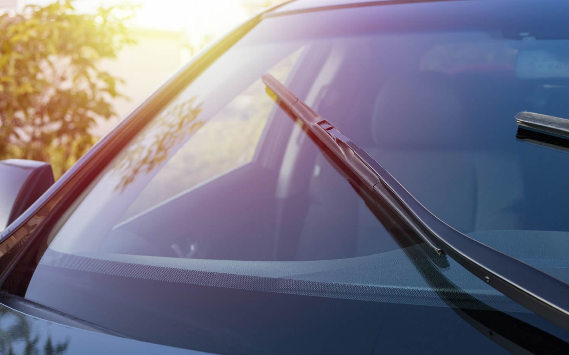 Windshield wipers on a car windshield with sunlight reflecting off the glass