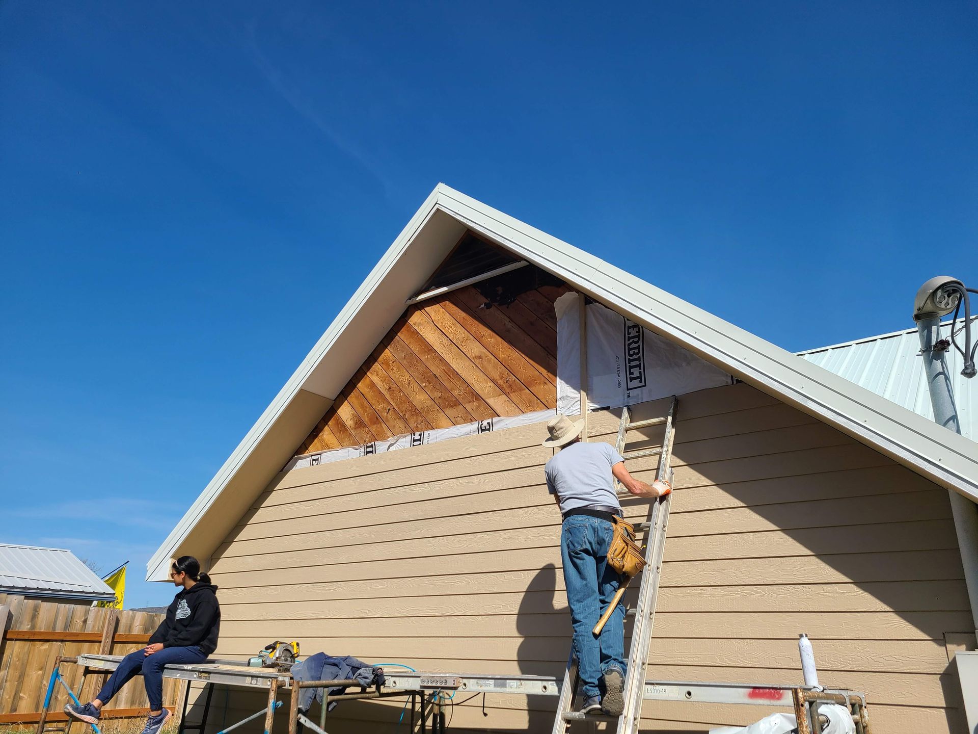 A man on a ladder putting up siding on the outside of a church