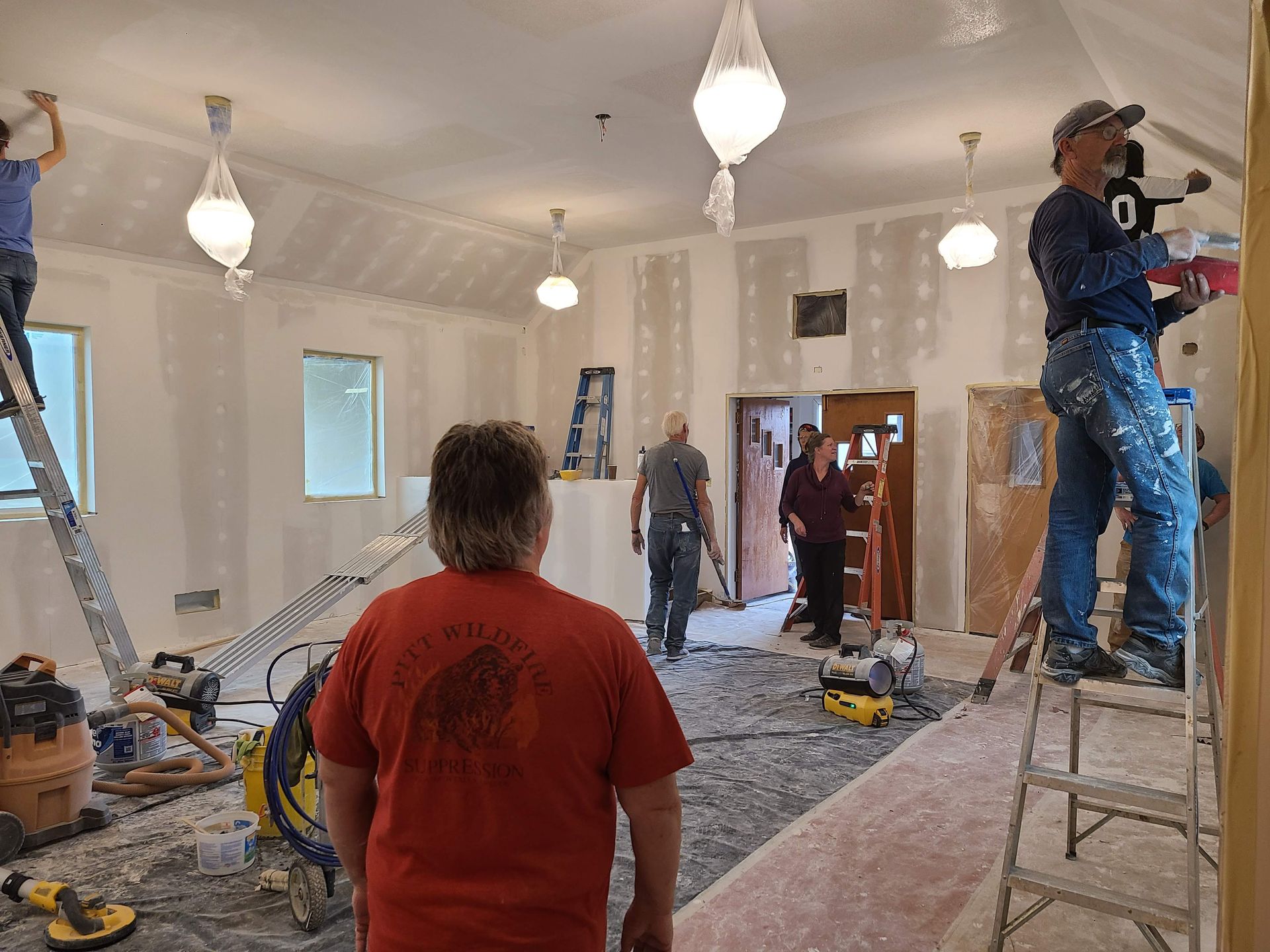 Volunteers work on ladders to paint the newly added drywall