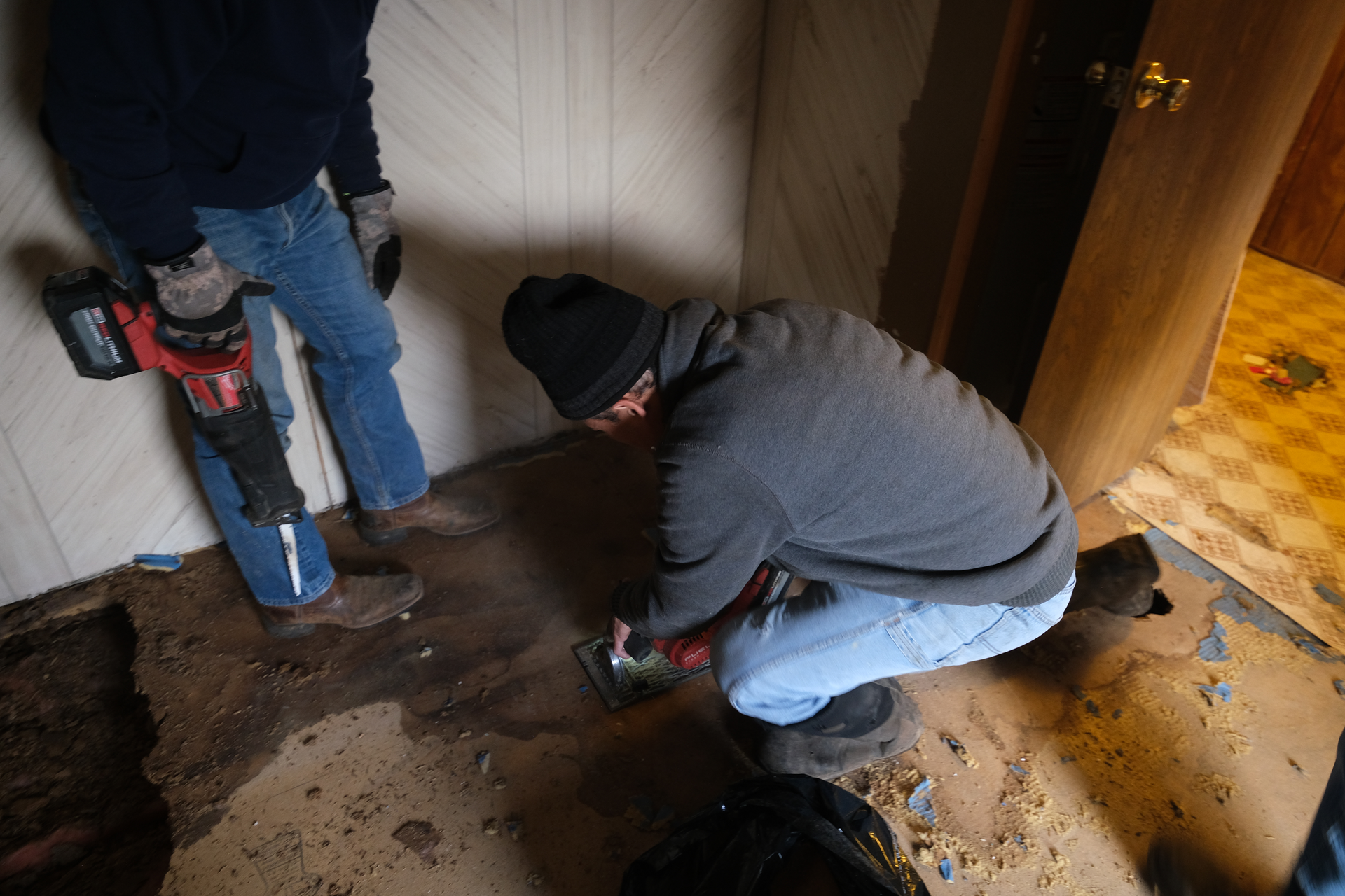 A man is kneeling down working with power tools to replace old flooring