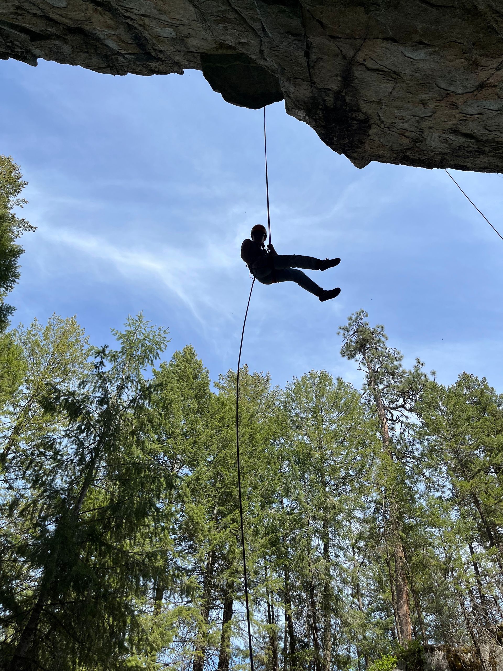 A person is hanging from a rope while rappelling off a rock wall