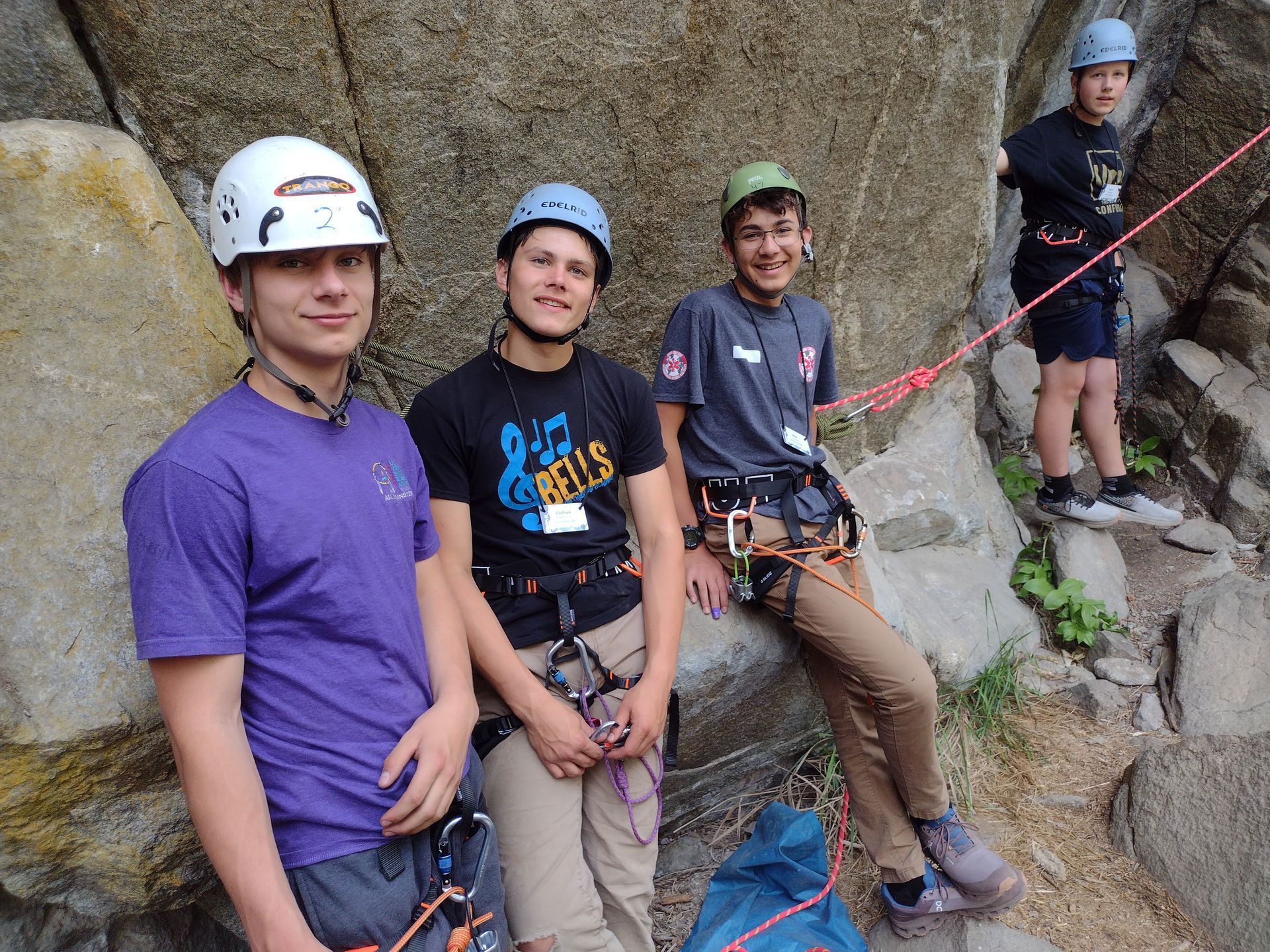 A group of harnessed young men are standing next to each other on a rock wall.