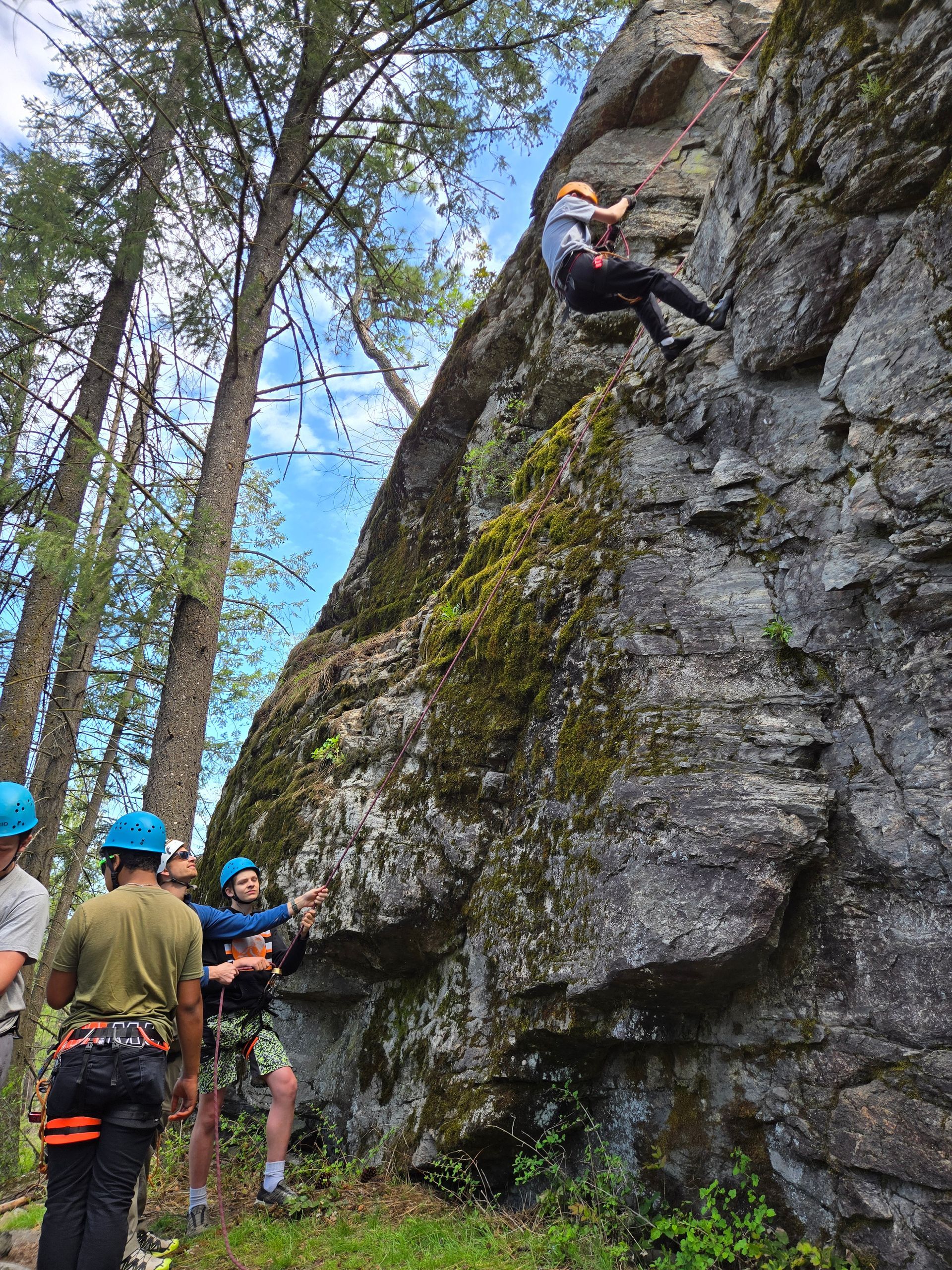 Teens at the base of a rock wall preparing to climb it.