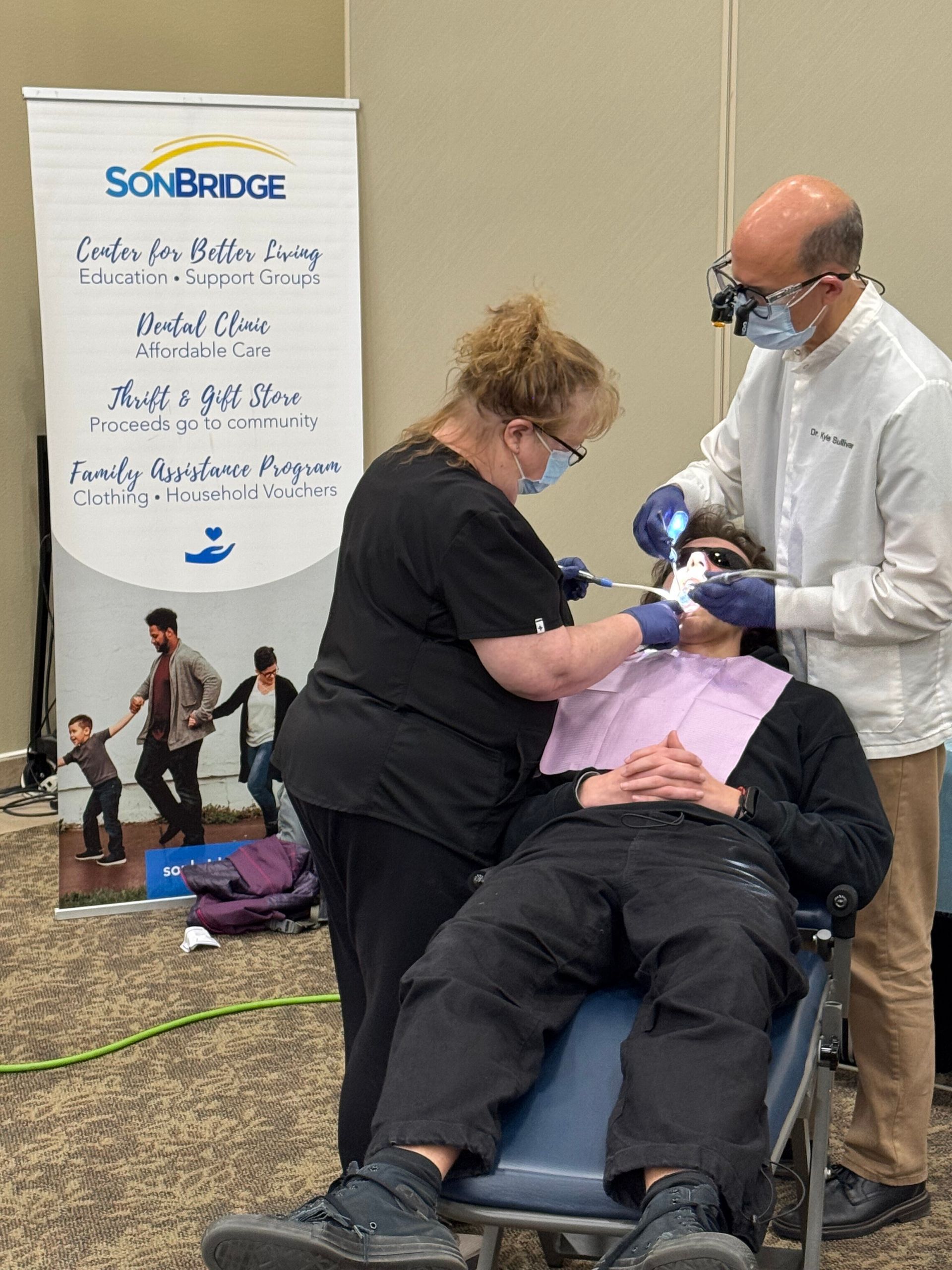 A man is getting his teeth worked on by a dentist assisted by Lorinda Sheldon.