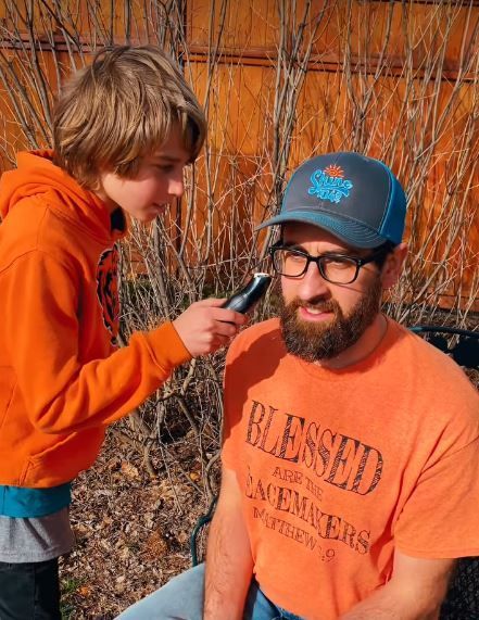 Shine 104.9 Chaplain Tyler Kern has his beard shaved off by one of his sons as part of a pledge goal